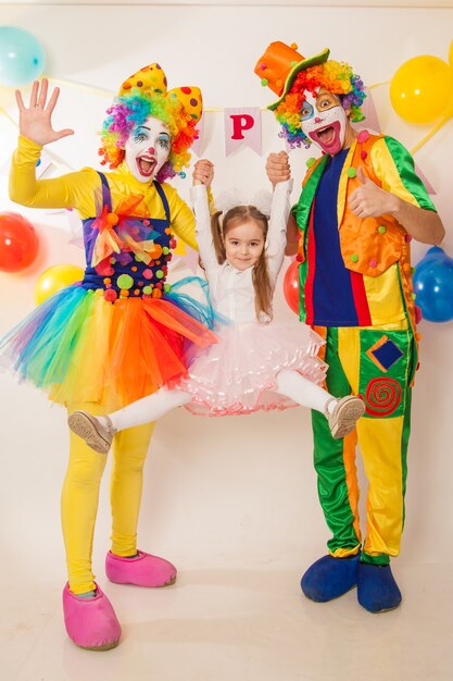 Cheerful emotional clowns on a holiday with a girl show emotions