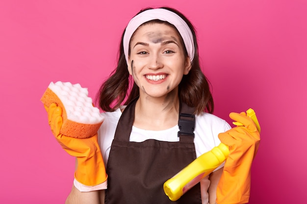 Cheerful energetic bright young woman looks happy isolated over pink in studio, ready to do general cleaning