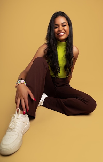 Cheerful ethnic female millennial smiling sitting in beige studio