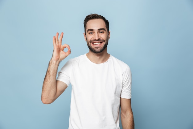 Cheerful excited man wearing blank t-shirt standing isolated over blue wall, ok