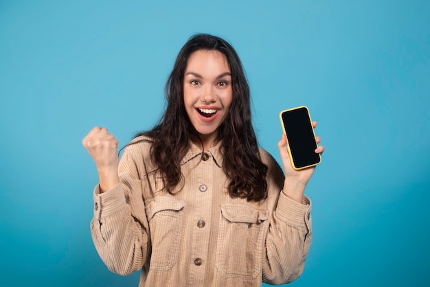 Cheerful excited millennial european lady student show phone with empty screen celebrate win