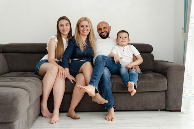 Cheerful family is sitting on the sofa at home bald father with a beard hugs his wife with childrenfamily concept family pastime