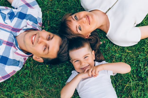 Cheerful family lying on grass in a circle and looking at camera.