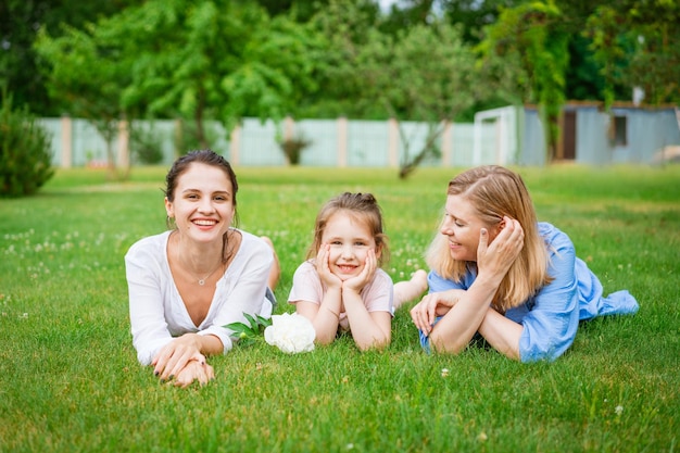 Cheerful family in park mom and daughter and grandmother lie on green grass