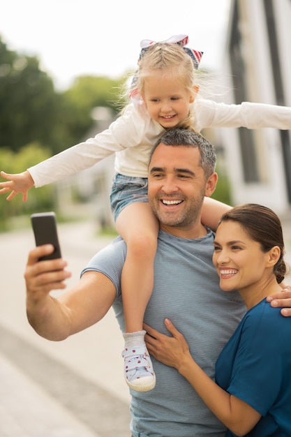 Cheerful family smiling. Cheerful family smiling while making selfie all together standing outside