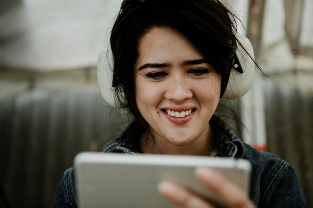 Cheerful female carpenter with protective headphones using a tablet at a workshop