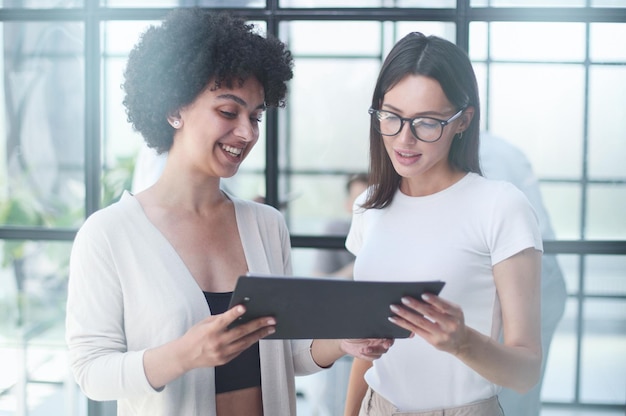 Cheerful female employees enjoying break Two women in formal clothes sitting in office lounge chatting and laughing