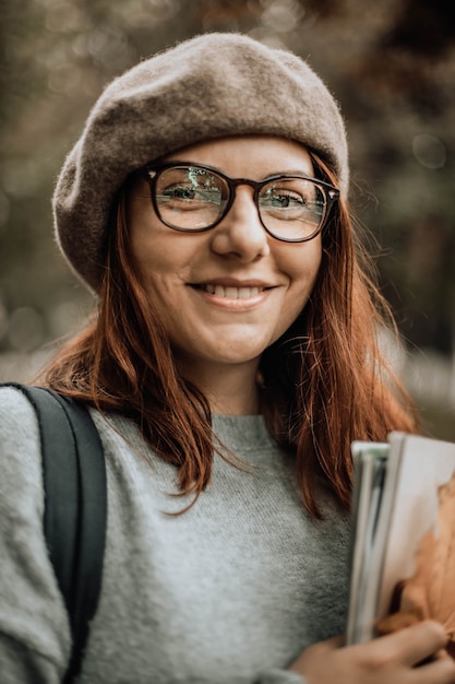 Cheerful female student in glasses looks at camera in the park