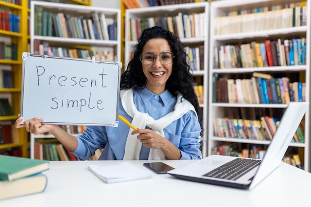 Cheerful female teacher holding a board with present simple written on it demonstrating english