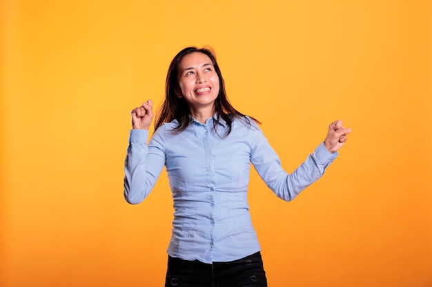 Cheerful filipino woman dancing and having fun during leisure time in studio over isolated background. Joyful smiling model enjoying showing her dance moves during work break. Entertainment concept