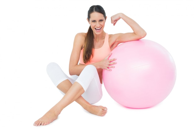 Cheerful fit woman flexing muscles by fitness ball