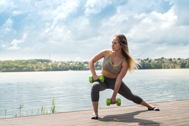 Cheerful fitness woman in sportswear exercising with dumbbell, outdoors. Healthy lifestyle