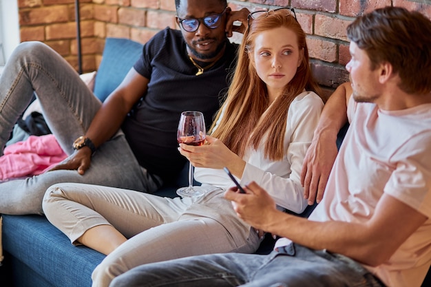 Cheerful friends sitting on sofa, toasting and having fun