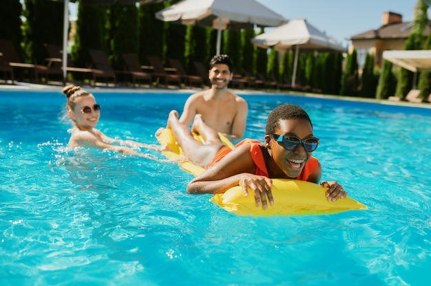 Cheerful friends swim on a mattress in the pool