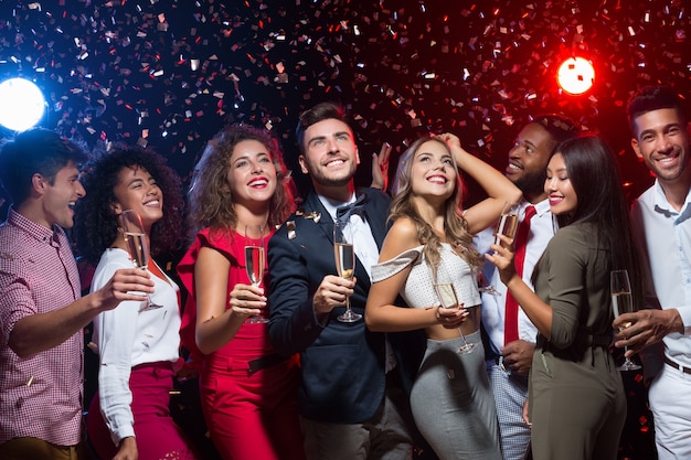 Cheerful friends with champagne flutes dancing at New Year party, smiling upwards at camera