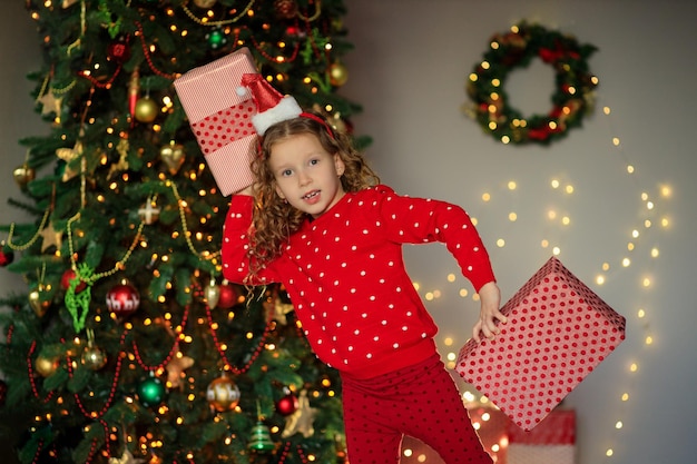 cheerful funny little girl baby with new year gifts by the tree