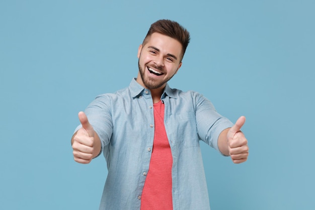 Cheerful funny young bearded guy 20s in casual shirt posing isolated on pastel blue wall background studio portrait. People sincere emotions, lifestyle concept. Mock up copy space. Showing thumbs up.