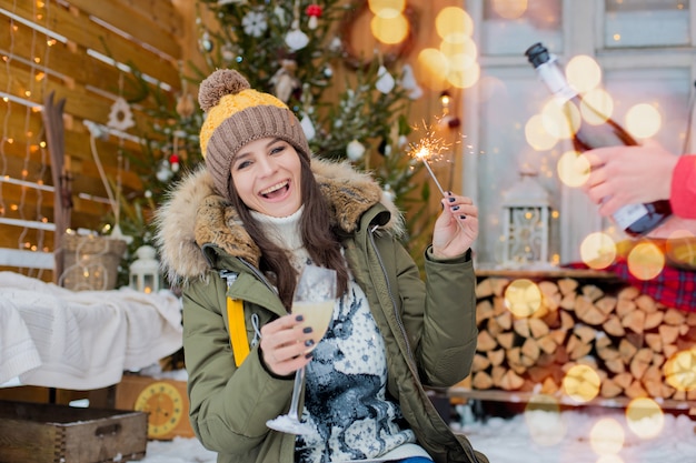 Cheerful girl hat  down jacket with sparklers with glass champagne in her hand celebrates 