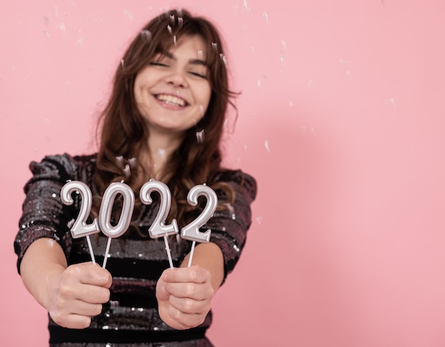 Cheerful girl on a pink background smiles and holds the numbers 2022 in her hands, celebrating the new year, copy space.