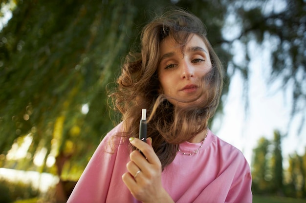 Cheerful girl in a pink t-shirt with an electronic cigarette in the park.