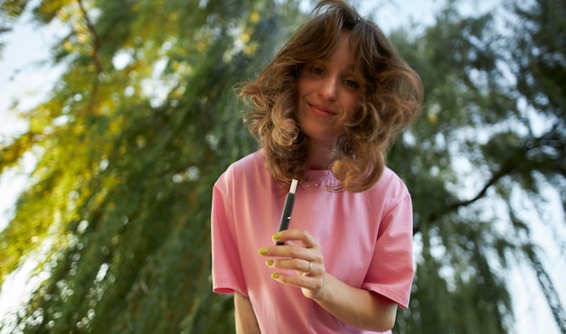 Cheerful girl in a pink t-shirt with an electronic cigarette in the park.