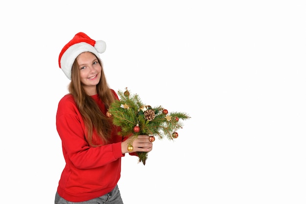 Cheerful girl in santa hat wearing red pullover with branches of christmas tree