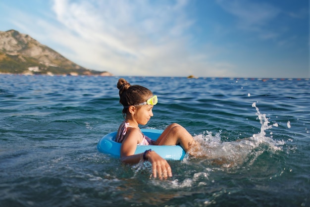 Cheerful girl sits in an inflatable circle and splashes with water in the sea