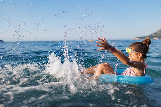 Cheerful girl sits in an inflatable circle and splashes with water in the sea