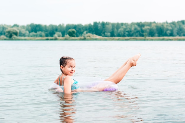 A cheerful girl swims on an inflatable ring in the river and stretches her legs Local tourism Summer vacation