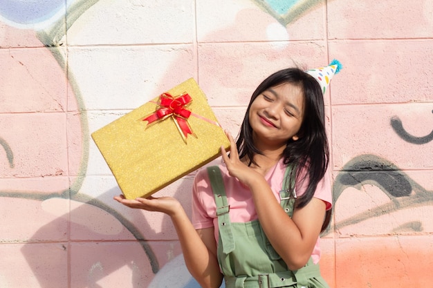 The cheerful girl wearing party hat with gift box sitting on colorful background