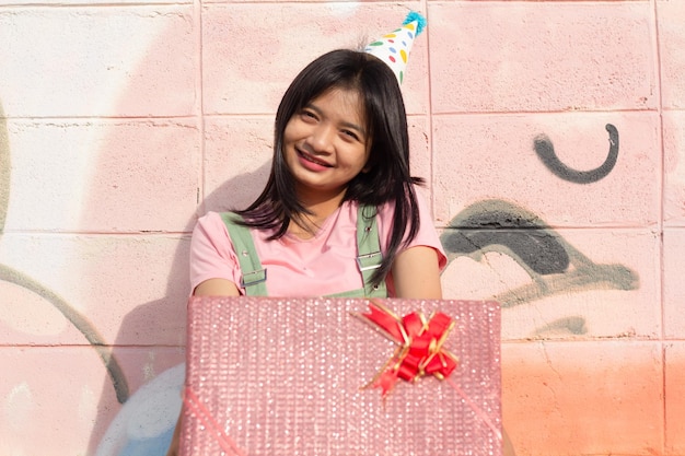 The cheerful girl wearing party hat with gift box sitting on colorful background