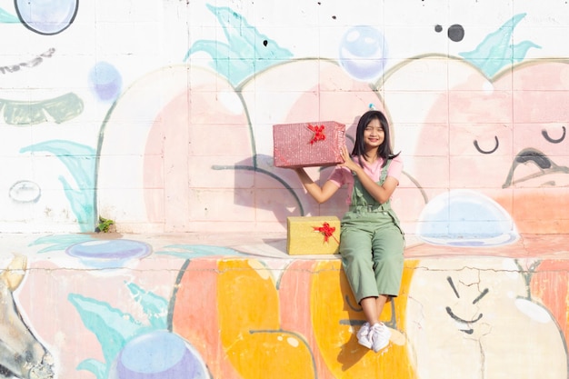 The cheerful girl wearing party hat with gift box sitting on colorful background