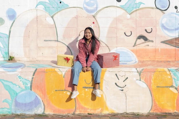 The cheerful girl wearing party hat with gift box sitting on colorful background