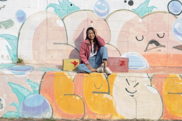 The cheerful girl wearing party hat with gift box sitting on colorful background