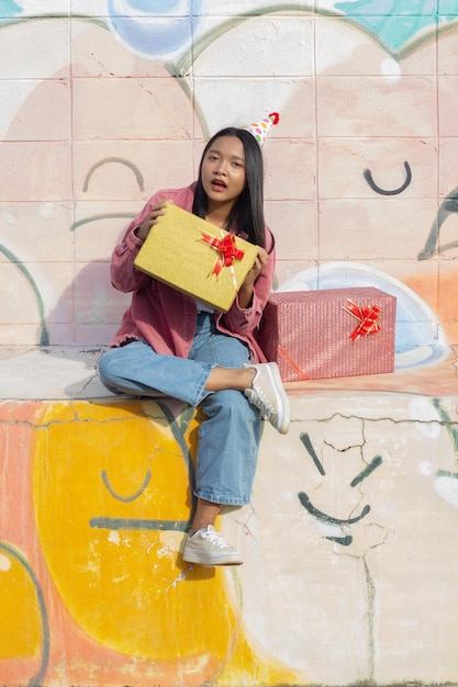 The cheerful girl wearing party hat with gift box sitting on colorful background