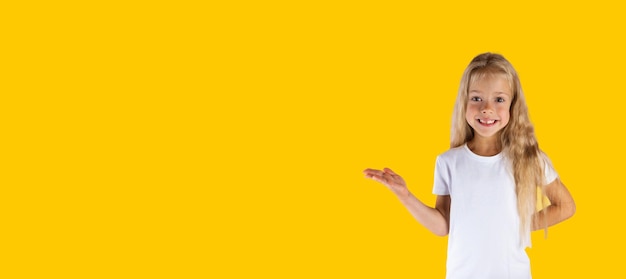 Cheerful girl in a white tshirt with outstretched hand isolated on a yellow background banner