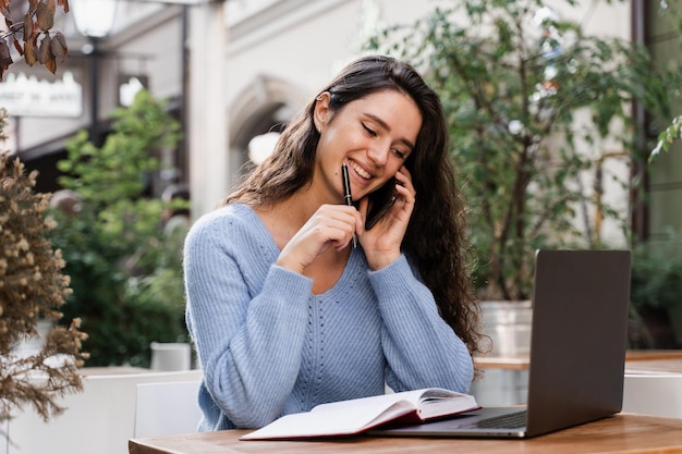 Cheerful girl with phone and laptop is working online with customers and chatting with team Busy business woman with laptop and phone is chatting and working remotely with colleagues