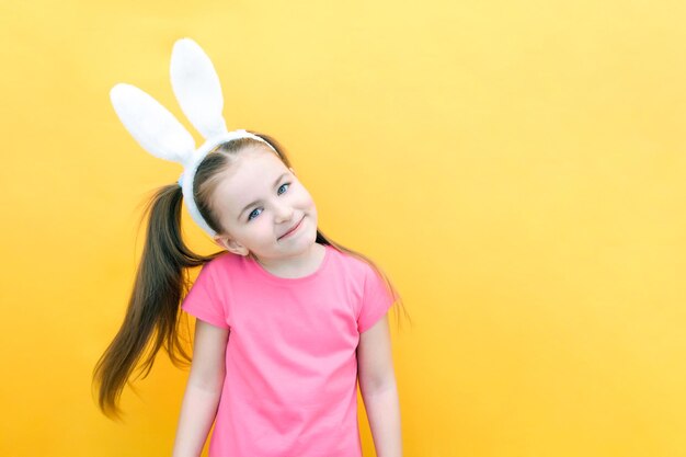 Cheerful girl with rabbit ears on her head on a yellow background. Funny crazy happy child. Easter child. Preparation for the Easter holiday. promotional items. copy space for text, mockup