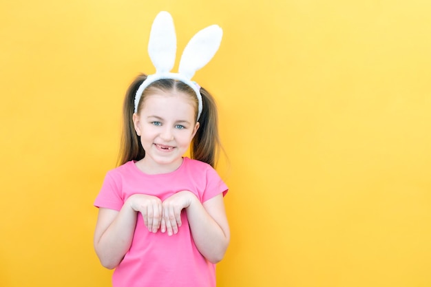 Cheerful girl with rabbit ears on her head on a yellow background Funny crazy happy child hands like a rabbit Preparation for the Easter holiday copy space for text mockup