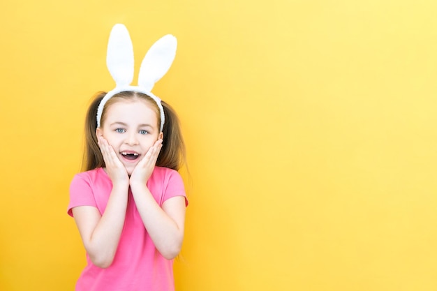 Cheerful girl with rabbit ears on her head on a yellow background Funny happy child emotion of surprise copy space for text mockup