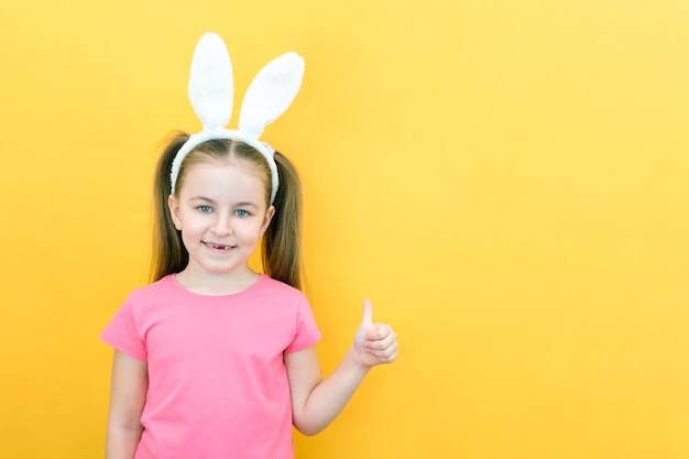 Cheerful girl with rabbit ears on her head on a yellow background Funny happy child shows like an empty space copy space for text mockup