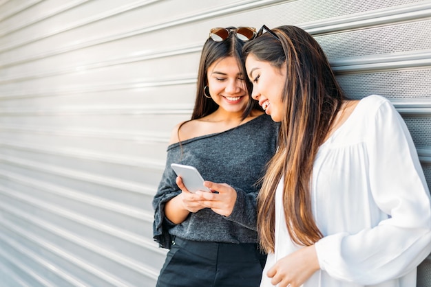 Cheerful girlfriends using smartphone on street