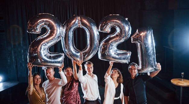 Cheerful group of people with drinks and balloons in hands celebrating new 2021 year.