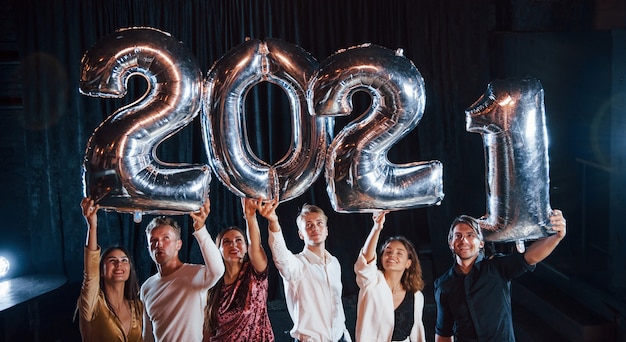 Cheerful group of people with drinks and balloons in hands celebrating new 2021 year.