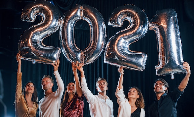 Cheerful group of people with drinks and balloons in hands celebrating new 2021 year.