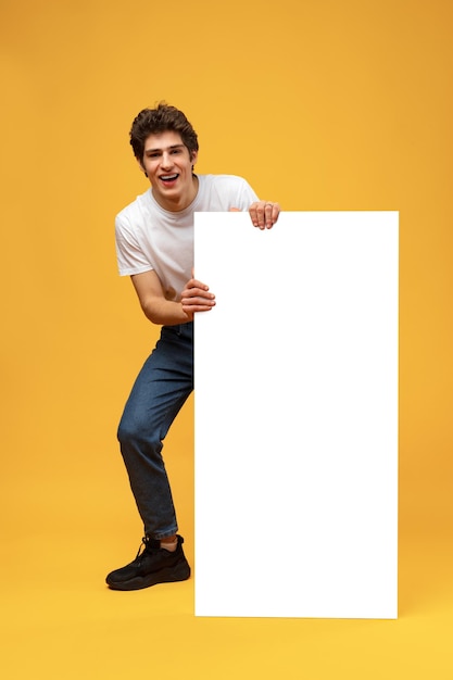 Cheerful guy demonstrate empty space blank offer on yellow background