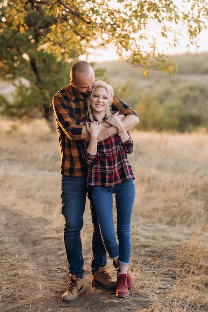 Cheerful guy with a board and a blonde girl for a walk in plaid shirts at sunset