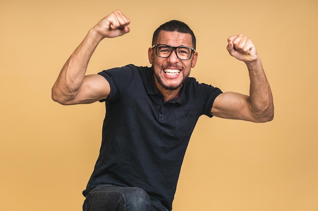 Cheerful handsome African american black man making yes gesture while excited about winning Ecstatic young fan rooting and expressing support Success concept isolated over beige background