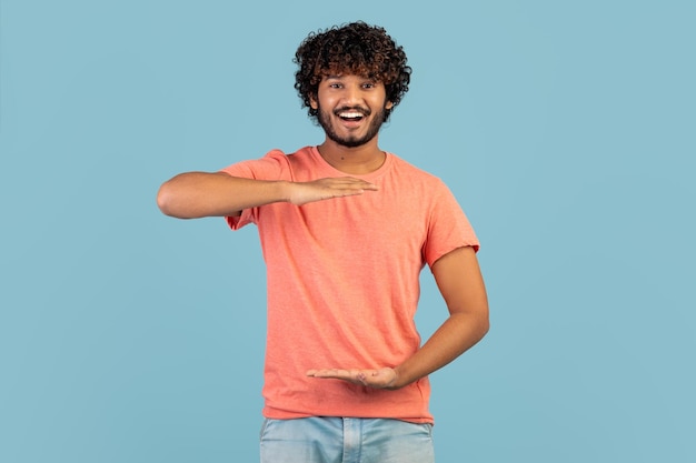 Cheerful handsome indian guy showing something invisible in his hands