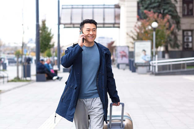 Cheerful and happy Asian businessman talking on the phone waiting for a plane and a taxi at a public transport stop